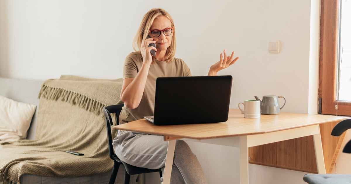 Woman sitting at a desk, using a laptop and smartphone while working from home